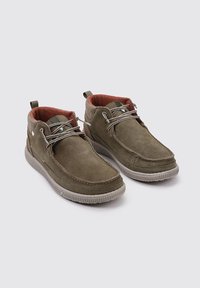 Botas de tobillo de ante verde oliva con forro de tela roja, suela de goma flexible, costuras blancas y acentos de cordones minimalistas en la parte frontal.