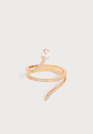 Bague spirale en or ornée de petites pierres claires et d’une plus grande pierre claire taille marquise à une extrémité sur un fond clair uni.