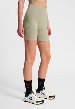 Licht olijfgroene fietsshorts met een hoge taille, textuurstof en een chevronpatroon aan de linkerkant. Gepaarde met zwarte sokken en witte sneakers.
