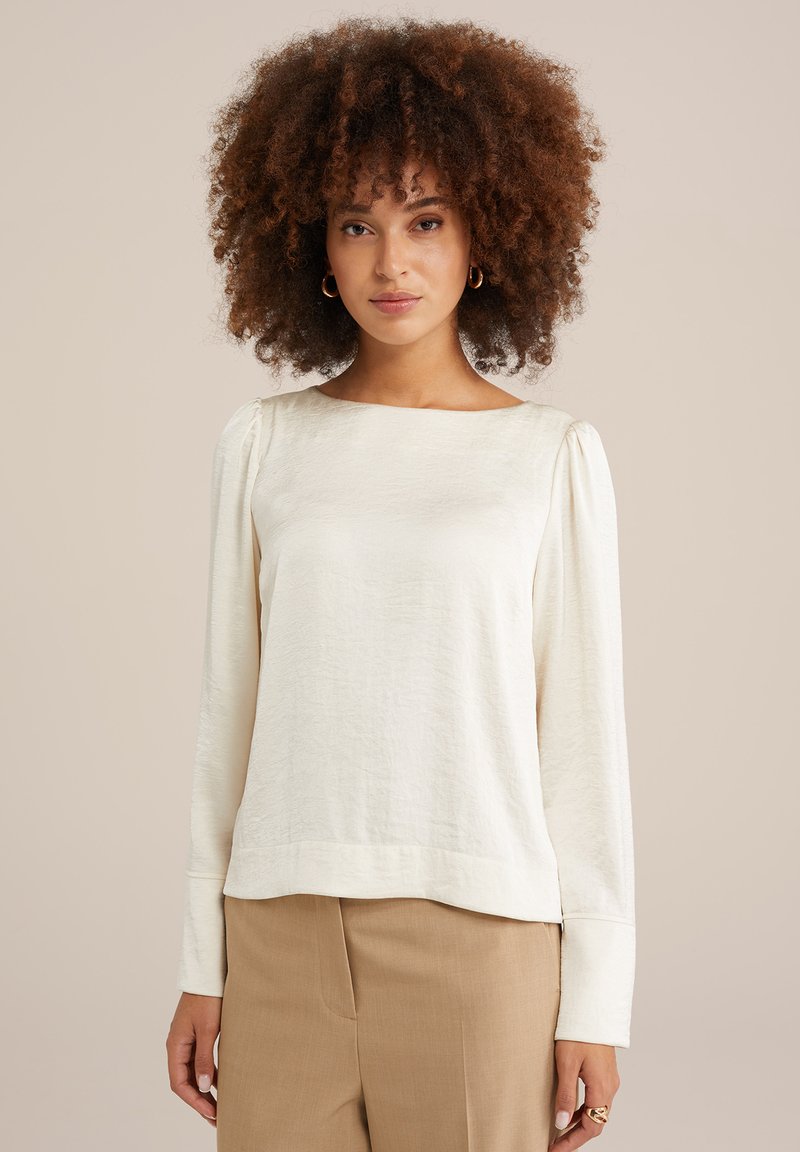 Top a maniche lunghe color crema con scollo quadrato, tessuto testurizzato e dettagli arricciati sulle spalle. Abbinato a pantaloni beige.