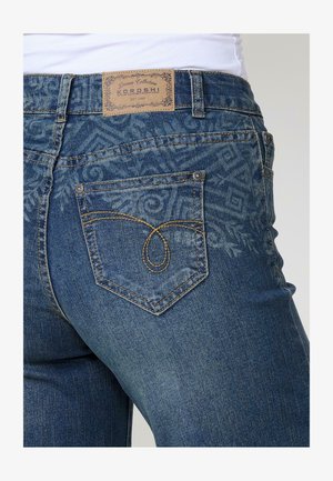 Dunkelblaue Denim-Jeans mit einem verblassten Muster. Verfügt über ein gebrandetes Leder-Patch, charakteristische Rückentaschen-Stickerei und Metallnieten.