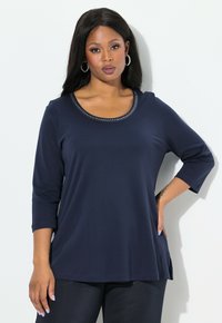 Marinblå långärmad topp med rundad halsringning och dekorativ pärlifestyle. Mjuk tyg med sidoflikar för ökad rörelsefrihet.