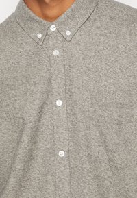 Graues Hemd aus strukturierter Stoffqualität mit klassischem Kragen und weißen Knöpfen, versehen mit einer Brusttasche.