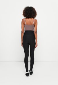 Brązowy, dopasowany top na krótki rękaw z cienkimi ramiączkami, w zestawieniu z wysokimi czarnymi legginsami. Legginsy mają gładką teksturę i elegancki krój.