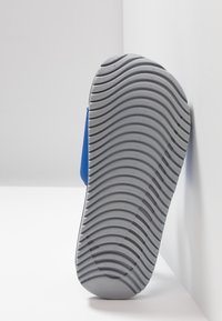 Blå sneaker med en teksturert grå gummisåle, med et bølgete mønster. Sidelaget er glatt, med et moderne design.
