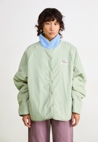 Lichtgroene oversized jas met een blauwe fleece kraag. Voorzien van drukknoopsluitingen en een label aan de linkerkant. Soepele textuur.