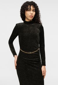 Μαύρο, μακρυμάνικο, εφαρμοστό φόρεμα από υφή υφάσματος με μεταλλική όψη, με λεπτομέρεια από χρυσή αλυσίδα στη μέση.