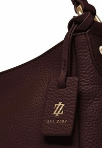 Borsa in pelle borgogna con una finitura testurizzata, caratterizzata da un'etichetta logo dorata con la scritta "EST. 2007" attaccata da un cinturino in pelle.