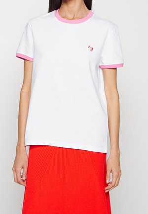 Femme portant un t-shirt blanc avec bordure rose aux manches et au col, petit logo chien sur la poitrine, assorti à une jupe rouge texturée.