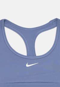 Primer plano de un sujetador deportivo azul de Nike con diseño de espalda nadadora y el logo de swoosh blanco de Nike en el centro frontal.