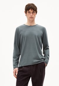 Langarmshirt aus sanftem grünem Baumwollstoff mit rundem Ausschnitt, lockerer Passform und glatter Textur, kombiniert mit dunklen Kordhosen.