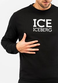 Felpa nera a maniche lunghe con grande testo bianco "ICE ICEBERG" sul davanti. Realizzata in un morbido tessuto testurizzato con scollatura arrotondata.