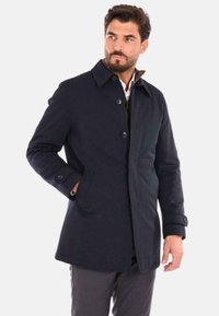 Cappotto blu navy con chiusura a bottone, ampio colletto e tasche laterali. Tessuto liscio con una vestibilità su misura e dettagli di cucitura minimi.