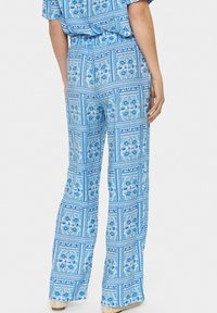 Mėlynos raštuotos platėjančios kelnės su elastinga juosmele, dekoruotos gėlių raštu ir tekstūruota medžiaga. Lengvos ir laisvai krentančios.