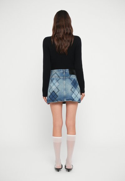 Minifalda de denim con un diseño de patchwork en varios tonos de azul, una cinturilla negra y un dobladillo deshilachado. La modelo lleva medias hasta la rodilla.