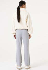 Suéter crema con un cuello alto, combinado con pantalones de chándal de pierna ancha en gris claro. El conjunto presenta texturas suaves y un ajuste relajado.