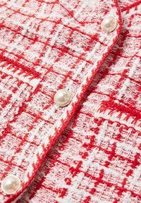 Tissu tissé rouge et blanc avec un motif pied-de-poule texturé et des boutons style perle sur un vêtement.