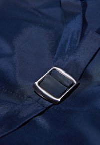 Marineblaues Gewebe mit glatter Textur zeigt eine metallische silberne Schnalle, die einen schwarzen Riemen sichert und das Verschlussdetail hervorhebt.