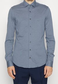 Lange mouw knoopshirt in lichtblauw, gemaakt van een gladde stof, met donkere knopen, een puntige kraag en een getailleerde pasvorm.