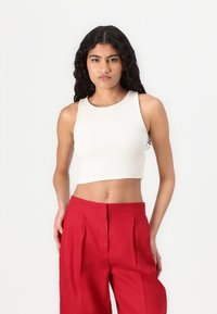 Top court côtelé couleur crème avec un décolleté rond et de larges bretelles, associé à un pantalon rouge taille haute plissé. Texture lisse.