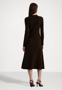 Brun stickad klänning med långa ärmar och en utsvängd nederkant, gjord av mjukt material. Kombinerad med svarta snygga högklackade skor.