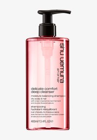 Shu Uemura schampo i en genomskinlig rosa flaska med en svart pump. Texten framhäver känslig komfort, fuktbalansering och viktiga ingredienser.