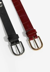 Fekete bőrszíj ezüstcsattal és piros lakkbőrszíj aranycsattal, mindkettő sima textúrával és klasszikus dizájnnal rendelkezik.