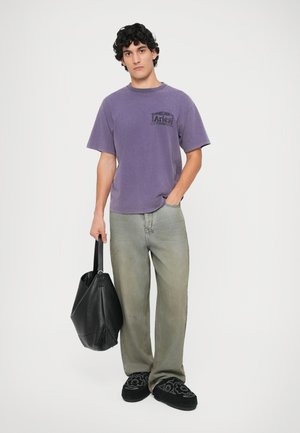 Lilla bomulds T-shirt med et sort Aries-logo, parret med lysegrå vide ben jeans, sort taske og sorte broderede slip-on sko.