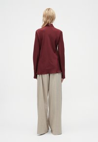 Burgunderfarbene Langarmbluse mit Kragen, kombiniert mit beigen weit geschnittenen Hosen. Glatte Stofftextur, minimalistisches Design ohne sichtbare Muster.