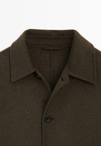 Manteau en laine vert olive foncé avec un col, doté d'une fermeture à boutons et d'un tissu doux et texturé. Détails de conception minimalistes.