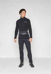 Svart fleece genser med halv-zip krage, kombinert med matchende svarte bukser. Har et brystlogo og en tettsittende midjepakke for praktisk bruk.