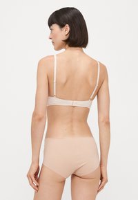 Nohavková súprava bezšvového podprsenkového kompletu v nude farbe, s nastaviteľnými ramienkami, mäkkým materiálom a jednoduchým dizajnom bez ozdôb.