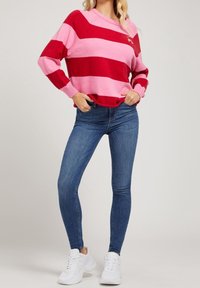 Pull rayé rouge et rose avec un col rond et des poignets côtelés, associé à un jean skinny bleu et des baskets blanches.
