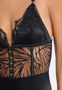 Body negro con detalles de encaje con patrones florales, tirantes ajustables y herrajes en tono dorado en el cierre frontal. Textura suave.