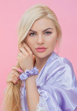 Lavendel Satinrobe mit Spitze, begleitet von einem passenden Haargummi. Das Model hat lange blonde Haare und einen rosa Hintergrund.
