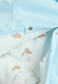 Lichtblauw baby kledingstuk met een gladde textuur, voorzien van een zachte binnenvoering bedrukt met kleine, bruine teddyberen. Drukknoopsluiting zichtbaar.