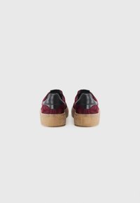 Baskets en suédine bordeaux avec des accents de talon en cuir noir et des semelles en caoutchouc texturé beige, dotées d'une languette pour un enfilage facile.