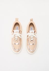 Et par beige og metallisk rosegull sneakers med hvite lisser og tykke hvite såler, sett ovenfra på en hvit bakgrunn.