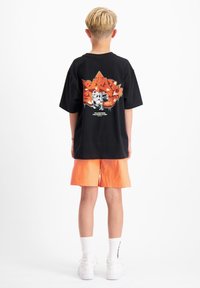 Zwart T-shirt met een kleurrijk grafisch ontwerp op de achterkant, gecombineerd met oranje shorts. De stof ziet er zacht en casual uit.