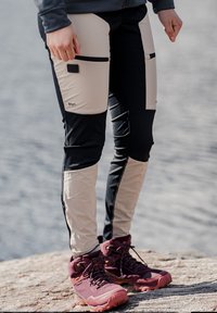 Svarta och beiga träningsbyxor med dragkedjefickor, tillverkade av hållbart material. Har texturerade paneler och en åtsittande design.
