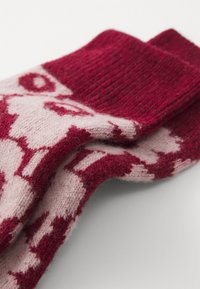 Calzini lavorati a maglia in un ricco bordeaux e morbido rosa. Presentano un polsino a coste e un motivo geometrico su tutta la superficie. Materiale in una calda e testurizzata miscela di lana.