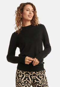 Black long-sleeve sweater with a crew neckline and ribbed cuffs, featuring a smooth texture and subtle shoulder detail. Styled with patterned pants.