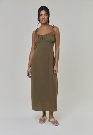 Olijfgroene midi-jurk met verstelbare bandjes, geplooide korset en een vloeiende rok. Gecombineerd met lichtbeige sandalen met versieringen.