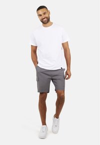 Biała koszulka z okrągłym dekoltem połączona z szarymi, wzorzystymi szortami cargo i białymi sneakersami. Szczególną cechą są boczne kieszenie w szortach.