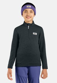 Felpa zip-up grigia scura con colletto alto e logo sul petto. Il modello indossa una fascia per capelli a maglia viola e nera. Pantaloni viola completano il look.