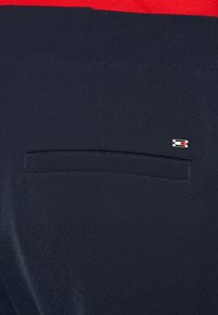 Jūrinės spalvos audinys su lygiu paviršiumi, turintis vieną galinį kišenę ir mažą, daugiaspalvį logotipo akcentą šalia kišenės.