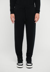 Black knitted jogger pants with an elastic waistband and drawstring. Features ribbed cuffs and a relaxed fit. Worn with black and white sneakers.