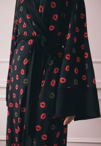 Sort slå-om-kjole med vide ærmer, bundet i taljen, med et mønster af røde og gyldne læbestiftmærker.