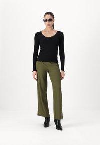 Haut noir à manches longues côtelé avec dentelle, associé à un pantalon large olive à rayures verticales. Bottines noires à talon pointu.