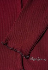Burgundska rebrasta dolga majica z raztrganimi manšetami. Na spodnjem delu ima srebrno vezenje "Pepe Jeans". Mehka tekstura tkanine.